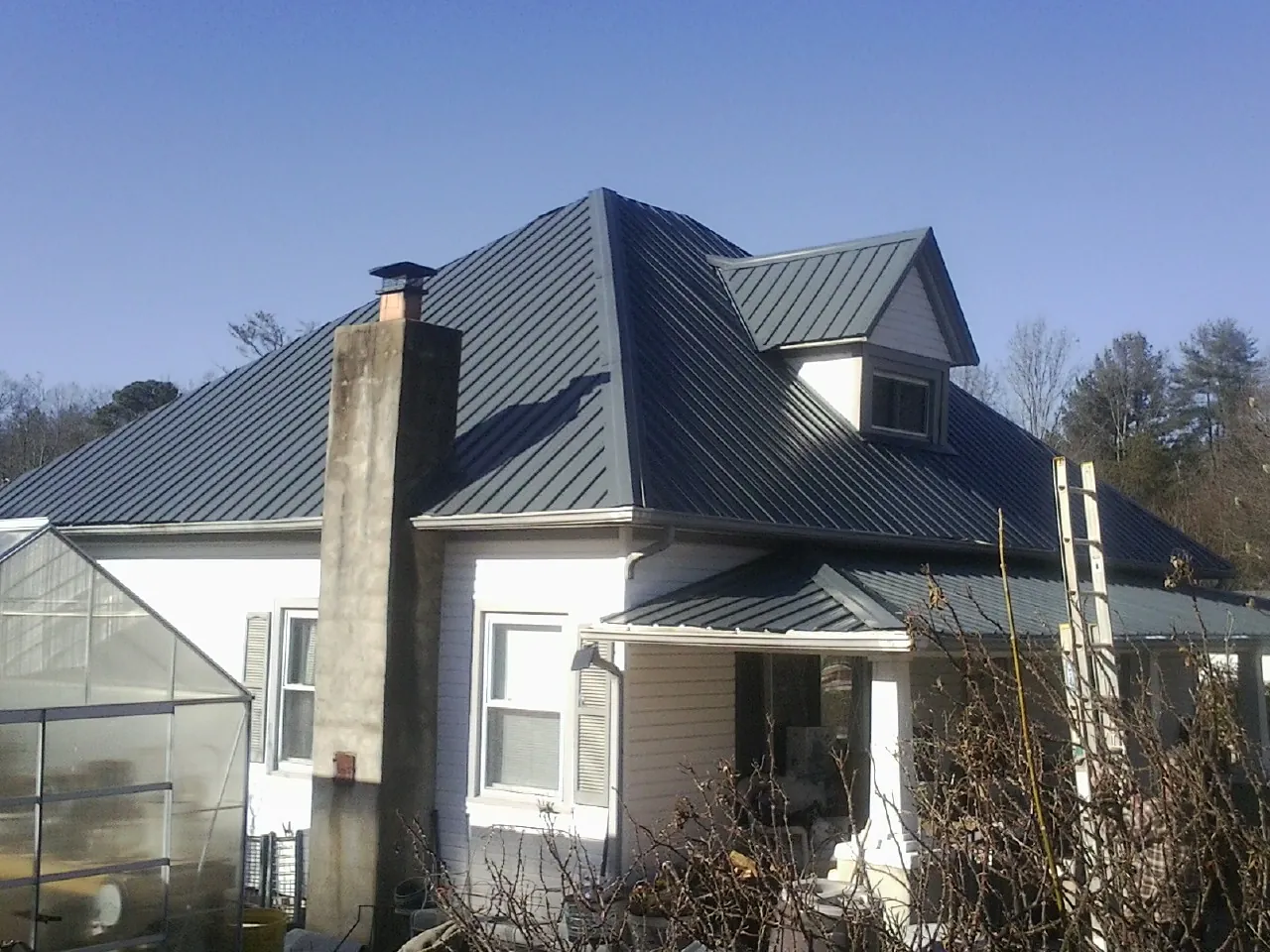 Dark blue standing seam metal roof on a white farmhouse with dormer — Slate & Tile Roof Repair by Roofing Brothers in West Camp