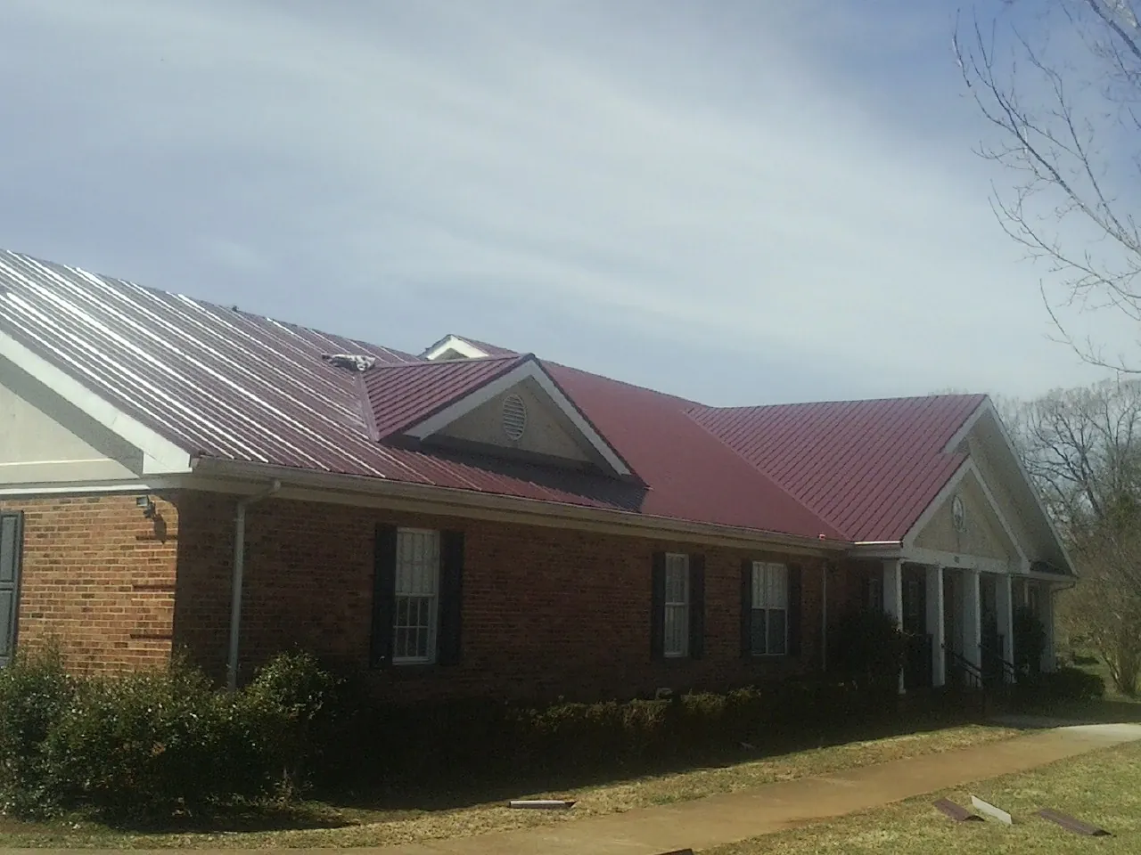 Red metal roof with gabled entries on a long brick building, from a Hail Damage Roof Repair job in West Camp