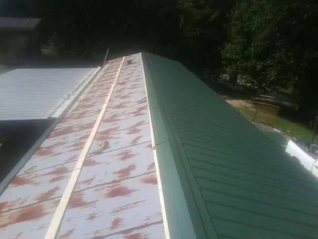 Old rusted panels beside newly installed green metal roofing — Wind Damage Roof Repair by Roofing Brothers in West Camp