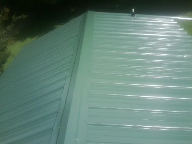 New green metal panels meeting at the ridge of a roof — Flat Roof Repair work by our crew in West Camp
