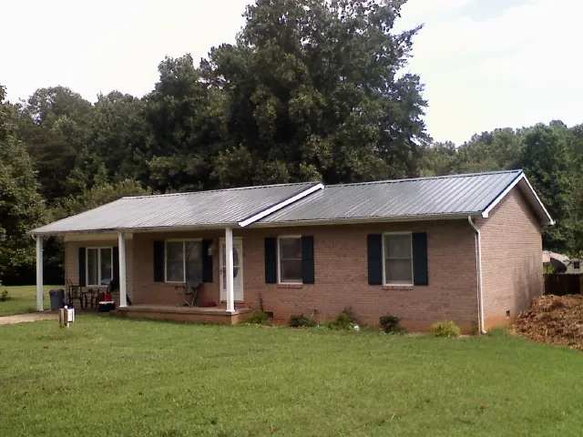 Gray metal roof on a brick ranch house with a side carport in West Camp