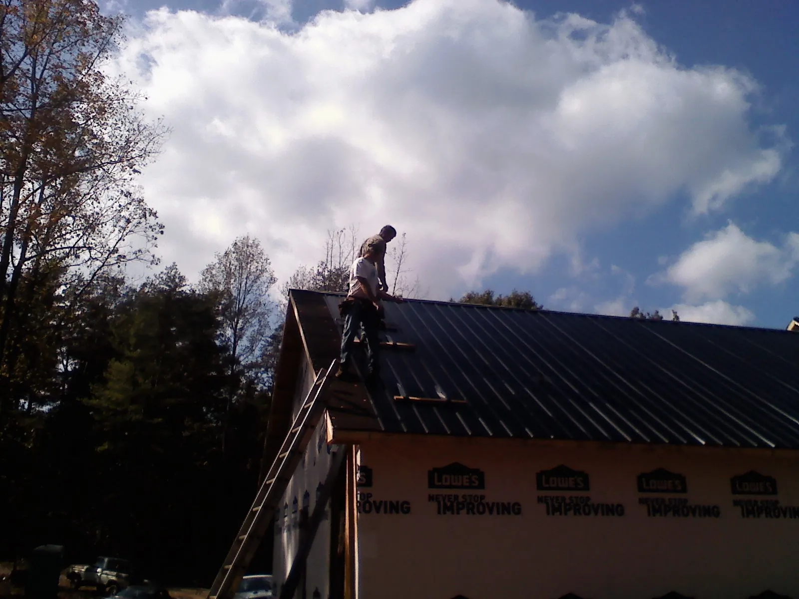 Roofer fastening dark metal panels high against a cloudy sky, from a Roof Inspection job in West Camp