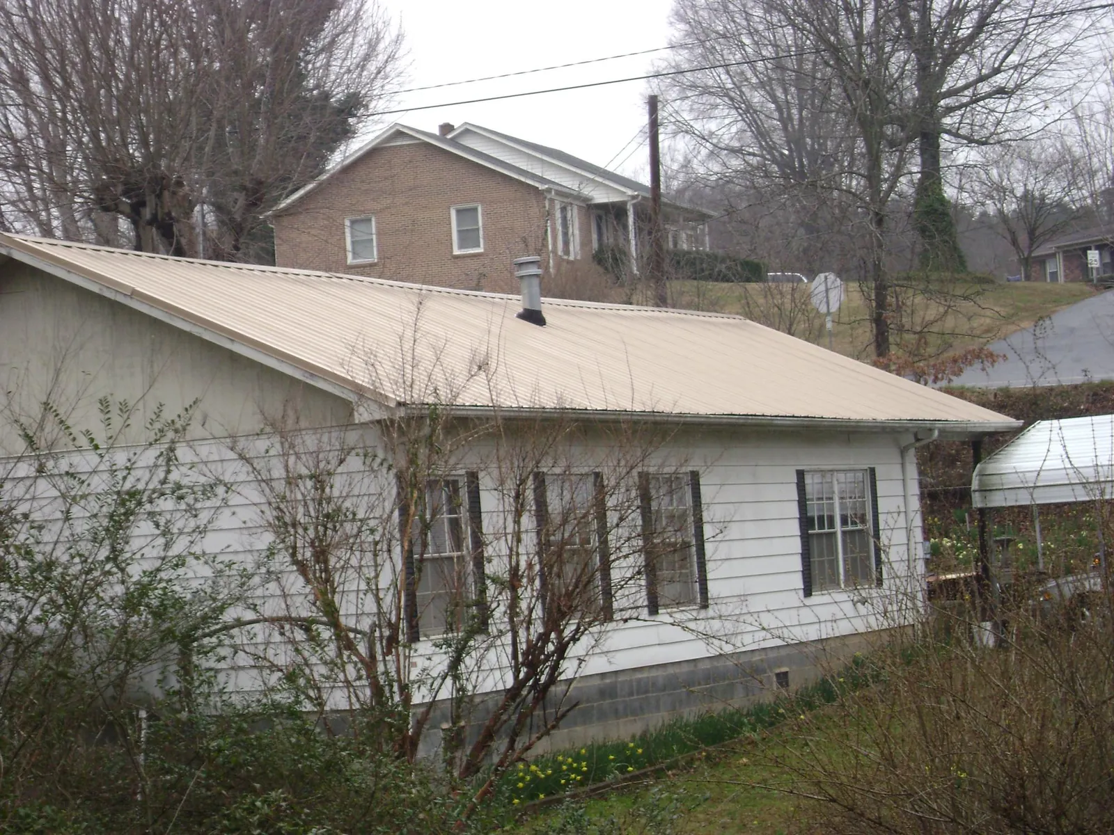 Tan metal roof on a white sided house set into a hillside — Commercial Roofing by Roofing Brothers in West Camp