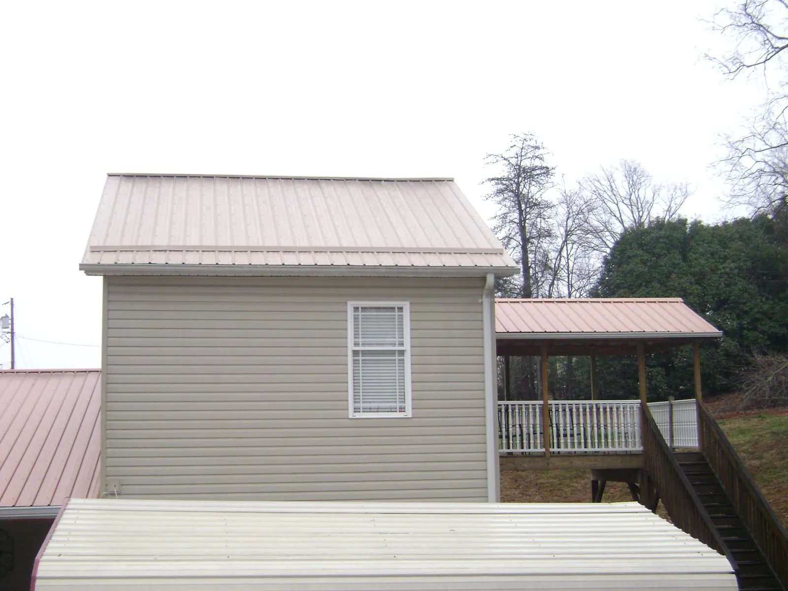 Tan metal roofs on a two story addition and attached porch, from a Roof Replacement job in West Camp
